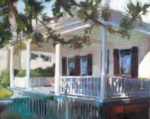 A white house with a wraparound porch and columns, shaded by leafy tree branches in sunlight.