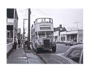 Vintage double-decker bus labeled “PRIVATE” parked on a street, people standing nearby, 1960s setting.