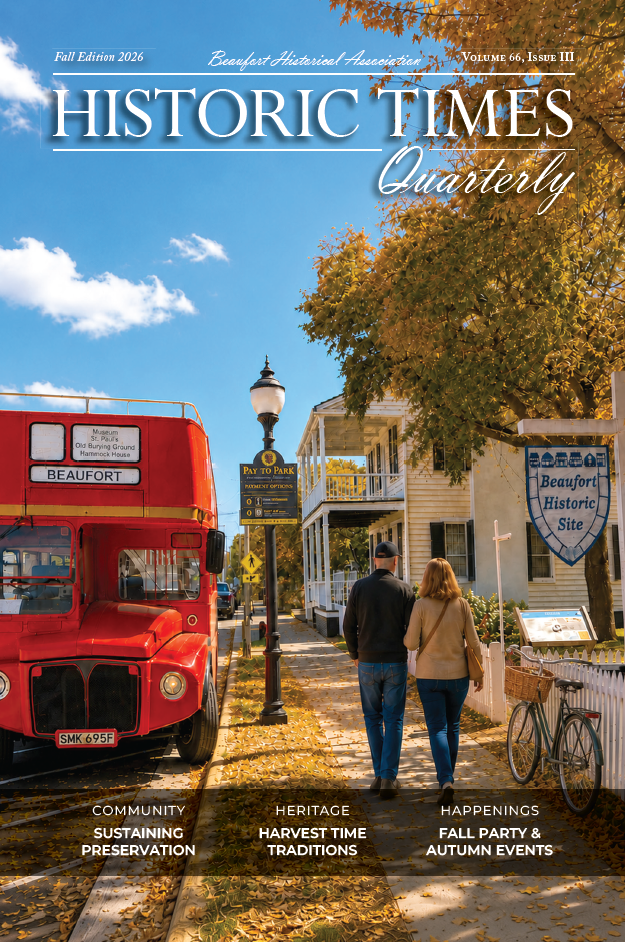 A couple walks past a red bus and historic houses with fall trees under a blue sky in Beaufort, North Carolina.